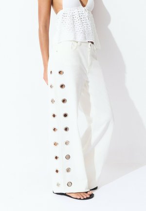 White wide-leg pants with metal grommet detailing along the side, featuring a smooth texture and a relaxed silhouette.