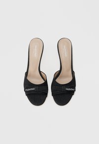 Sandalias deslizantes de denim negro con una suela suave y un acento de cinta prominente. Presentan un logo en el lateral y un diseño de espalda abierta.