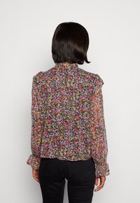Blouse met bloemenprint op een zwarte achtergrond met roze, paarse en gele bloemen. Lange mouwen met gerimpelde manchetten, knoopsluiting aan de achterkant.