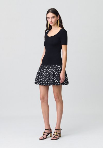 Haut noir à manches courtes avec un col rond et une jupe noire à motif floral. La jupe est évasée avec des détails froncés. Escarpins noirs à lanières.