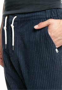 Námořnické pruhované kalhoty vyrobené z látky s bílými šňůrkami. Obsahují boční kapsu a kovové prvky na koncích šňůrek.