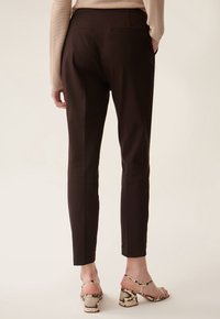 Pantalons ajustés marron avec une texture lisse, deux poches arrière et une coupe à la cheville ; associés à des sandales à talons block texturées et à brides.