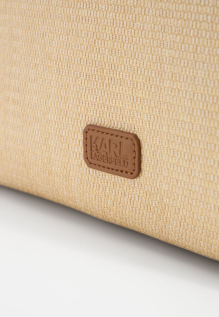 Beiger, strukturierter Stoff mit einem kleinen braunen Lederpatch, auf dem das „Karl Lagerfeld“-Logo geprägt ist, auf der Oberfläche einer Tasche.