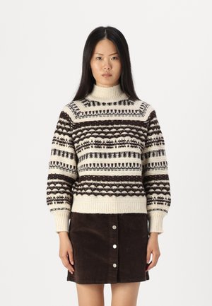 Pull en tricot avec une base crème et des motifs géométriques bruns, col montant et poignets côtelés. Associé à une jupe en velours côtelé marron.