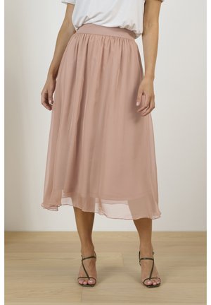 Roze chiffon midirok met elastische tailleband, vloeiende silhouet en een doorschijnende textuur, gecombineerd met groene sandalen met bandjes.