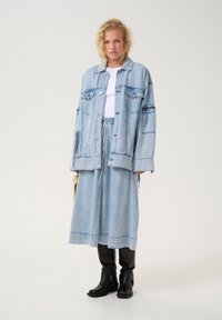 Hele halli denim oversized jakk koos esikotidega, sobitatud vastava denim seeliku ja mustade nahast põlvekõrguste saabastega, mis täiendavad välimust.