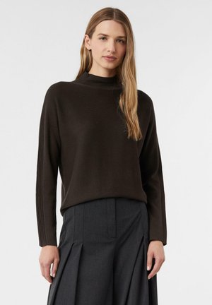 Dunkelbrauner, gerippter Strickpullover mit hohem Kragen und langen Ärmeln, kombiniert mit dunklen, gefalteten Hosen. Glatte Textur und lockere Passform.