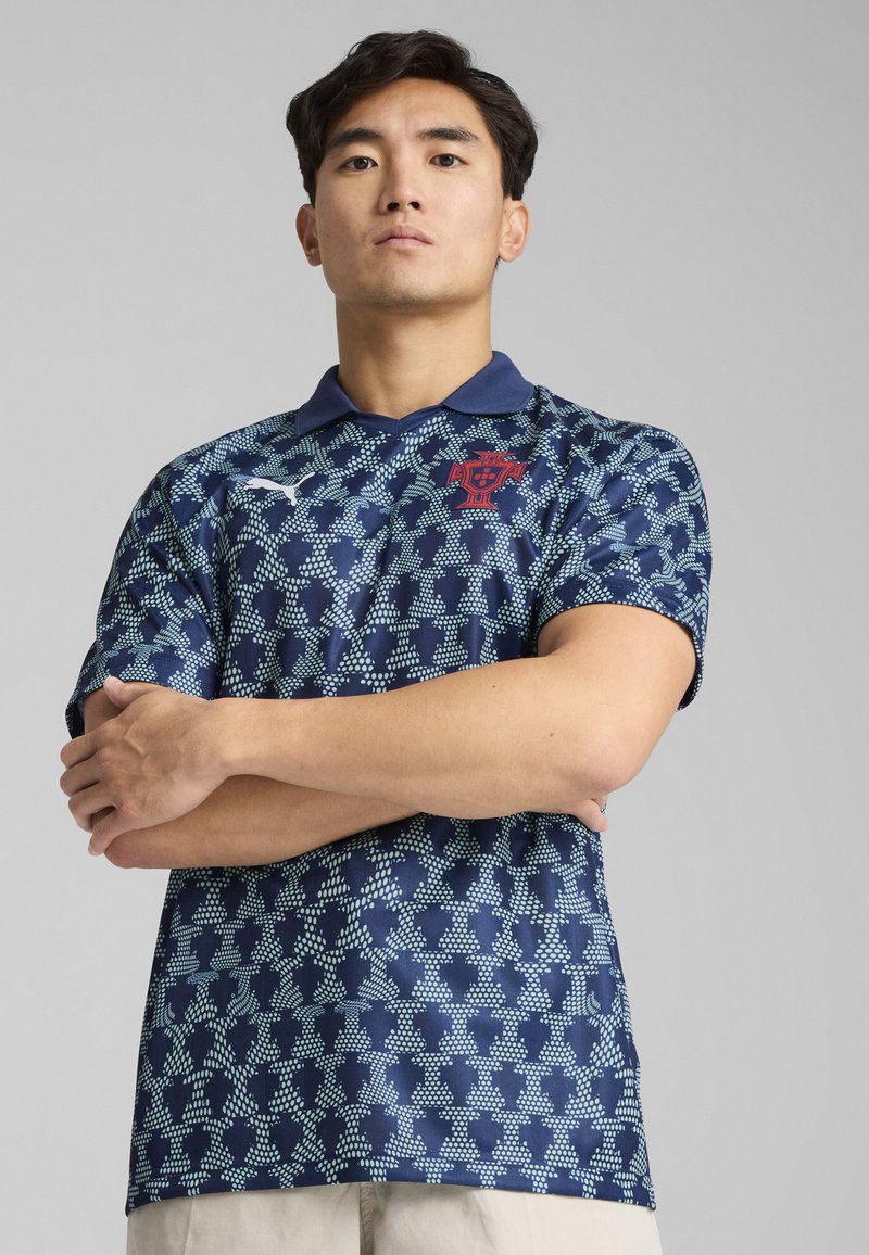 Polo shirt bleu marine avec un motif géométrique texturé en bleu et blanc, doté d'un col et d'un emblème rouge sur la poitrine.