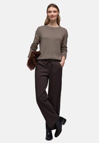 Pull vert olive, col rond, manches longues. Pantalon marron, taille élastique avec cordon de serrage. Bottines noires à talon léger.