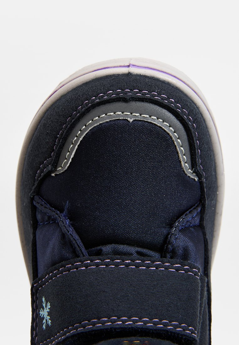 Dunkelblaue Sneaker mit einem plüschigen Obermaterial, grauem Zehenbereich, lila Nähte und einem Klettverschluss; mit einem kleinen weißen Schneeflockenmotiv.