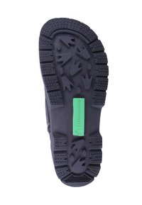 Suela de zapato de goma negra con una superficie texturizada y patrones de relieve multidireccionales, y una etiqueta de logo verde que dice "El Naturalista".