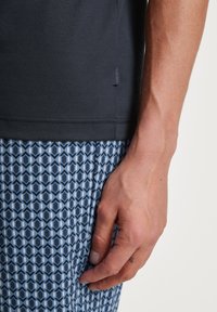 Black short-sleeve shirt with a soft texture, paired with patterned blue shorts featuring a geometric design and visible stitching details.