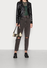 Černá kožená motorkářská bunda přes zelený krajkový top, v kombinaci s tmavě šedými roztrhanými džíny a černými robustními mokasíny. Dr�ží vzorovanou kabelku.