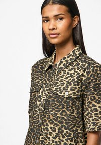 Camicia con stampa leopardata in una combinazione di colori beige e nero, dotata di colletto, maniche corte e due tasche frontali con chiusura a scatto.