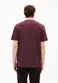 Korte mouwen, ronde hals t-shirt in diep bordeaux katoen. Gladde textuur met een rechte snit, voorzien van een klein label aan de onderkant.
