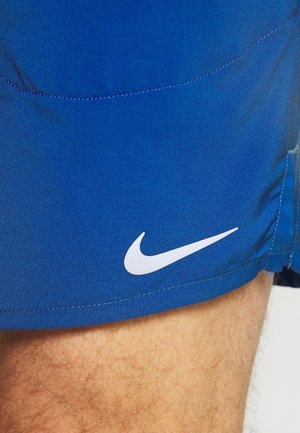 Blå atletiske shorts lavet af glat stof, med et hvidt Nike-logo på den nederste side. Designet har rene syningsdetaljer.
