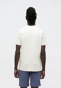 Világos bézs pamut rövid ujjú póló kerek nyakkivágással. Puha anyagnak tűnik, laza szabással, sötétkék rövidnadrággal párosítva.