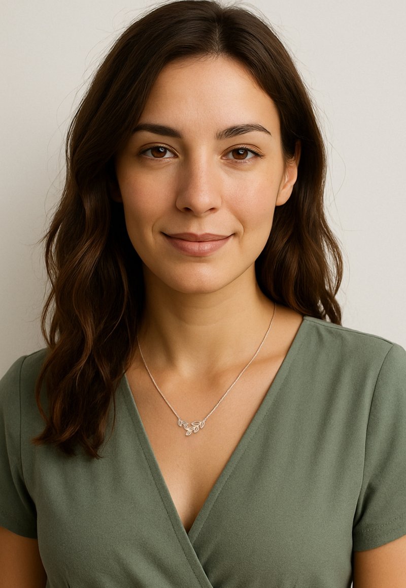 Sølvblad halskæde på en kvinde med mellembrunt hår, iført en grøn indpakningsbluse. Halskæden har delikate bladformede detaljer.
