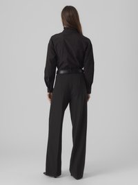 Maglietta nera a maniche lunghe con colletto arricciato, abbinata a pantaloni neri a vita alta e gamba larga, texture liscia, design minimalista.