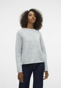 Maglione grigio chiaro in un tessuto morbido e testurizzato. Presenta un collo rotondo, maniche lunghe a raglan e un orlo leggermente accorciato. Indossato con jeans scuri.