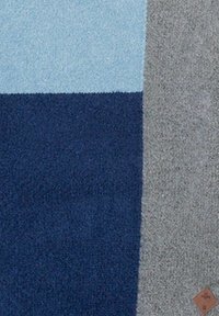 Manta texturada con bloques de color azul, marino y gris. Material suave con un brillo sutil, que incluye una pequeña etiqueta marrón en la esquina.