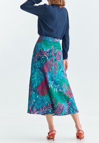 Falda midi con estampado floral en vibrantes tonos azules y verdes, con una cinturilla alta y tela suave. Combinada con sandalias de tacón alto rojas.