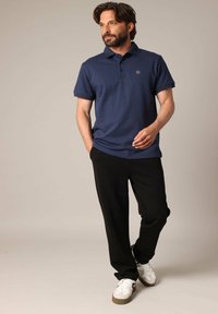 Polo shirt marine à manches courtes avec un design texturé, assorti à un pantalon noir et des baskets blanches avec des accents marron.