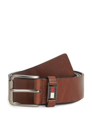 Cintura in pelle marrone con fibbia metallica argentata, arrotolata, con una piccola etichetta rettangolare con il logo Tommy Jeans vicino alla fibbia.