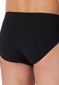 Schwarze Baumwollslips mit körpernahem Schnitt, ausgestattet mit einem weichen Bund und nahtlosen Kanten für höchsten Komfort. Glatte Textur ohne sichtbare Muster.