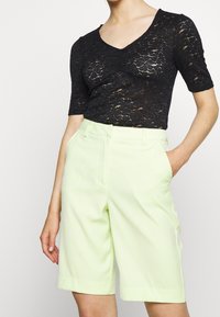 Svart spetsblus med korta ärmar och V-ringning, ihop med ljusgröna skräddarsydda shorts med sidofickor och en slät yta.