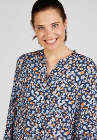 Navy button-up shirt with a colorful, abstract pattern in orange, blue, and white. Soft fabric with a relaxed fit and a banded collar.