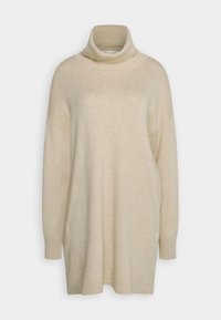 Béžový svetr s rolákem, dlouhými rukávy, volným střihem a žebrovanou texturou. Má vysoký límec a boční rozparky na spodním lemu.