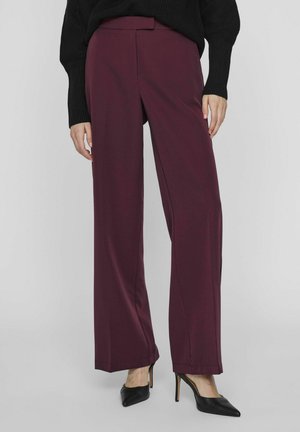 Pantalones de pierna ancha burdeos hechos de una tela suave, con una cintura ajustada y un pliegue delantero, combinados con tacones negros de punta.