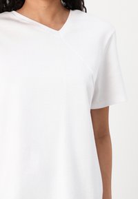 T-shirt bianca realizzata in morbido cotone, con scollatura a V e maniche corte, caratterizzata da un dettaglio di cucitura diagonale sulla parte anteriore.