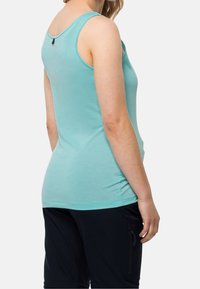 Una camiseta sin mangas de color azul claro, hecha de un material suave, con un escote redondeado y una etiqueta en la parte posterior. Combinada con pantalones cortos oscuros.