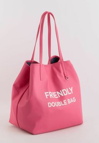 Bolso tote rosa hecho de material texturizado, con dos asas largas y texto blanco que dice "BOLSA DOBLE AMIGABLE".