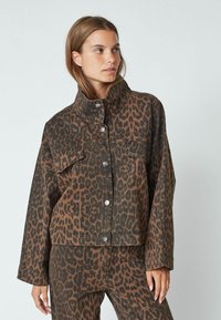 Brown leopard print jacket with a high collar, button closure, and two front pockets. Made of denim with a relaxed fit and long sleeves.