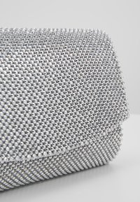 Borsa a pochette argentata coperta di piccoli strass luccicanti; presenta una chiusura a patta e una texture liscia con una forma strutturata.