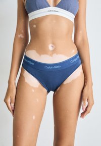 Coada de bumbac navy bikini cu un brâu elastic lat care prezintă logo-ul "Calvin Klein". Textură netedă, design cu talie joasă și fără modele.