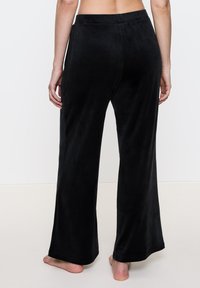 Zwarte, brede broek van zacht, glad materiaal met een elastische tailleband en geen zichtbare zakken, gezien van de achterkant.