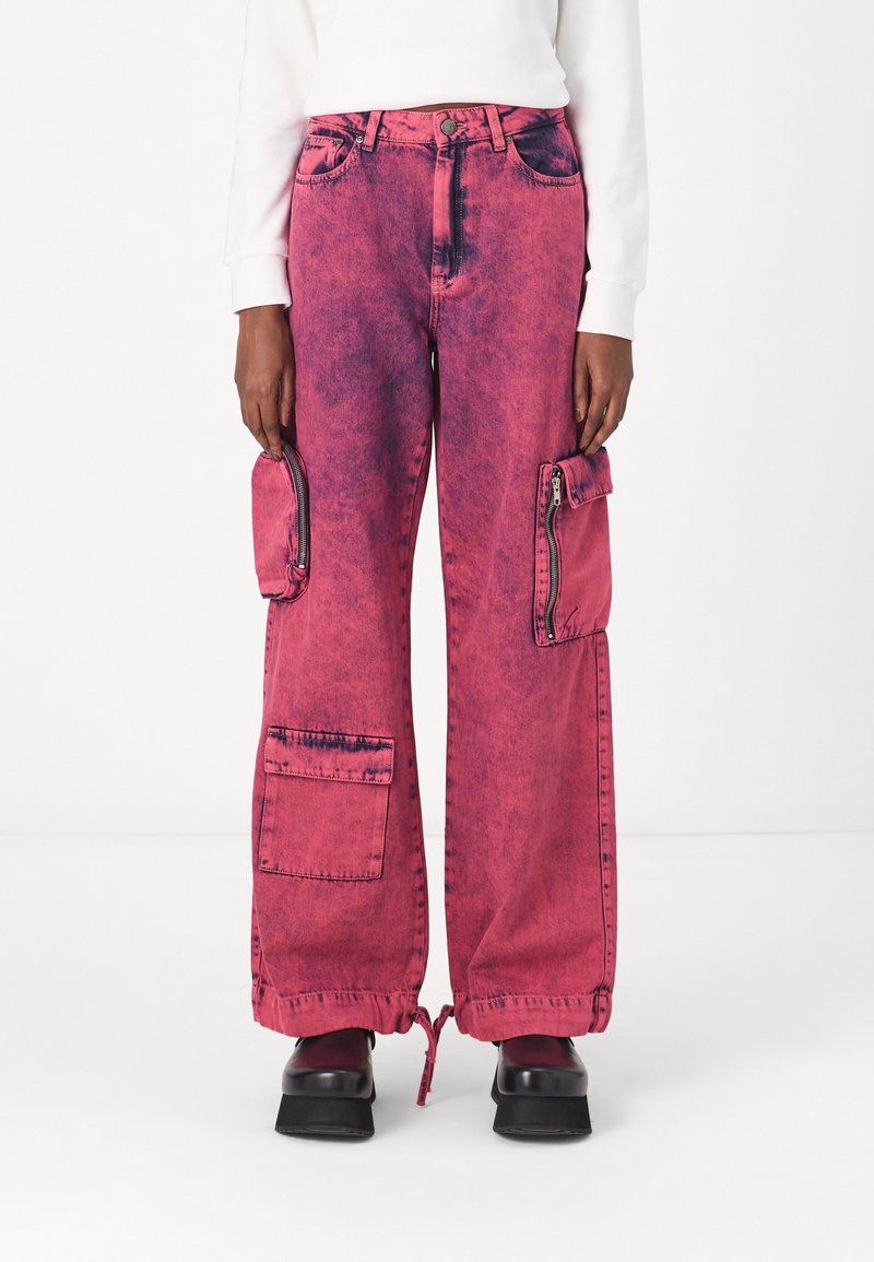 Pantalons cargo en denim rose avec une texture décolorée, présentant de grandes poches latérales, des fermetures éclair et des ourlets à cordon de serrage. Design à jambes larges.