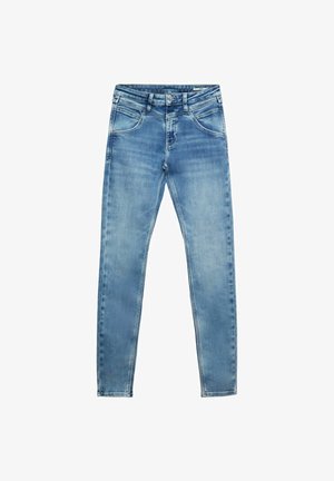 Slim fit licht vervaagde blauwe spijkerbroek gedragen met zwarte sandalen en een wit cropped topje, waarbij de buik zichtbaar is en de handen ontspannen langs de zijkanten hangen.