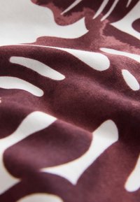 Gros plan d’un tissu froissé avec motif abstrait de feuilles bordeaux et blanc.