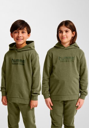 Två barn står sida vid sida och bär matchande olivgröna hummel sportkläder med hoodies och byxor, ler och tittar lite bort från kameran.