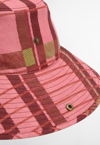 Chapéu bucket em tecido de padrão xadrez rosa, apresentando tons de castanho e verde, com riscas texturizadas e um detalhe de ilhós em latão para ventilação.