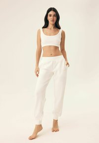 White cropped tank top with a gathered waist paired with matching white joggers featuring side pockets and elastic cuffs. Soft fabric texture.