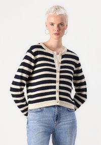 Striped cardigan in navy and cream, knitted texture, round neck, front button closure, with five golden buttons, paired with light blue jeans.