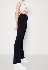 Zwarte flare jeans van denim, met een middelhoge taille en subtiele stiksels. Gepaard met witte sneakers.