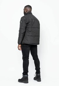 Svart puffjacka med hög krage och horisontell sömnad, i kombination med svarta jeans och svarta snörkängor. Minimalistisk design, utan accenter.