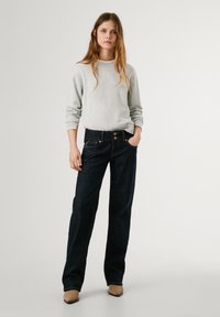 Svetlo siva pulover, temno modri široki džinsi z dvema sprednjima žepoma in kontrastnim šivanjem, v kombinaciji s bež visokimi petami.